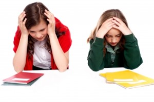 frustrated child and parent sitting down with their hands on their heads and notebooks in front of them