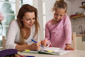 Mother helps her daughter do her homework at a kitchen table