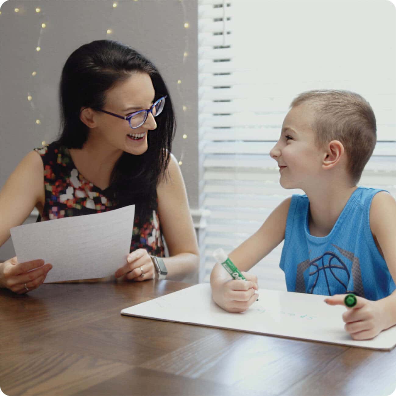 Woman helping young child with online dyslexia therapy reading program on laptop at table 