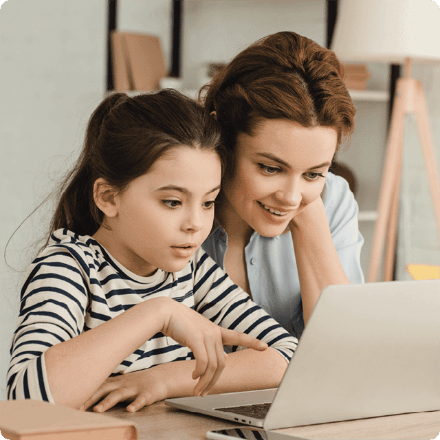 Woman helping young child with online dyslexia therapy reading program on laptop at table 