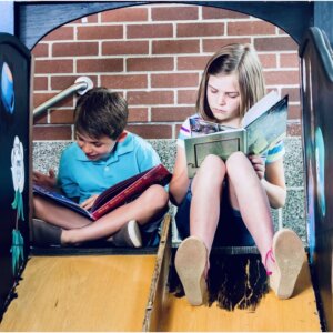 A brother and sister read books next to teach other while sitting on the floor