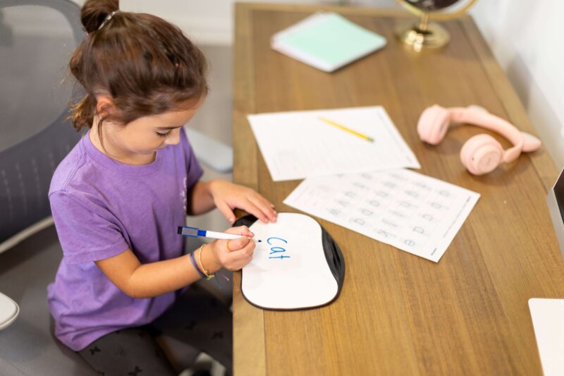 child writing word cat on whiteboard