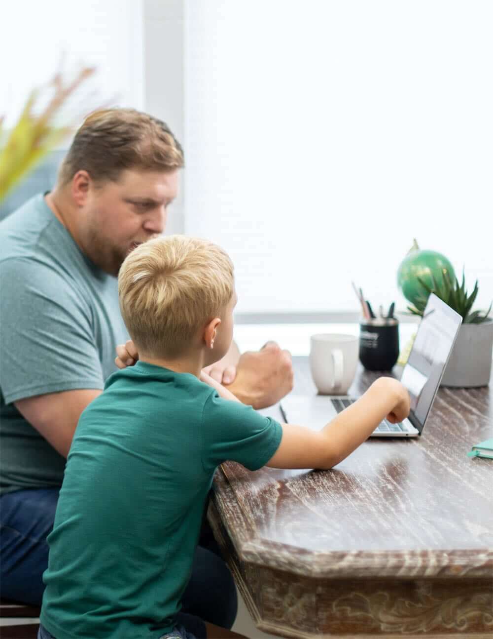 Dad helps his son take a reading and spelling inventory assessment test on a laptop